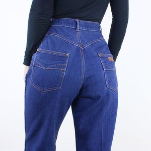 May include: A pair of high-waisted blue denim jeans with a straight leg fit. The jeans have a classic five-pocket design with a brown leather patch on the back right pocket.