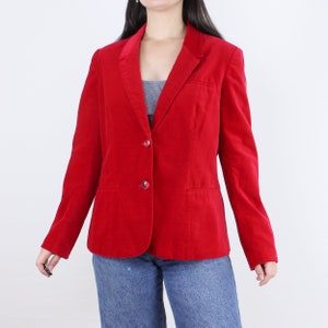 May include: A red velvet blazer with a classic notched collar and two button closure. The blazer has two flap pockets and long sleeves.