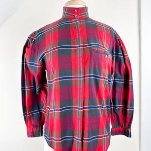 May include: A red, blue, and green plaid long-sleeve shirt with a high collar and a button-up front.