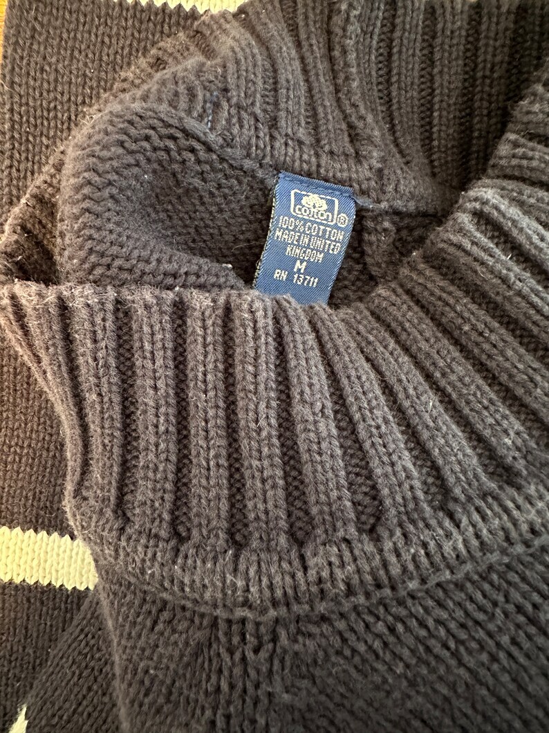 May include: A black and white striped sweater with a blue tag that reads "100% cotton made in United Kingdom M RN 13711".