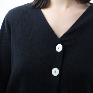 May include: A black long-sleeved shirt with a v-neck and three white buttons down the front.