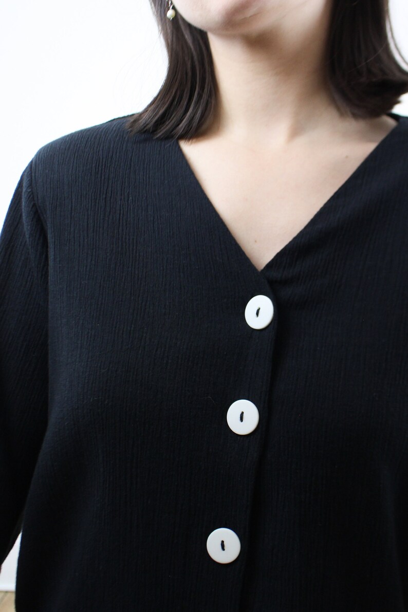 May include: A black long-sleeved shirt with a v-neck and three white buttons down the front.