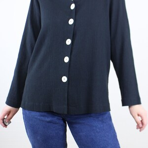 May include: A black long-sleeved button-up shirt with a v-neck and white buttons.