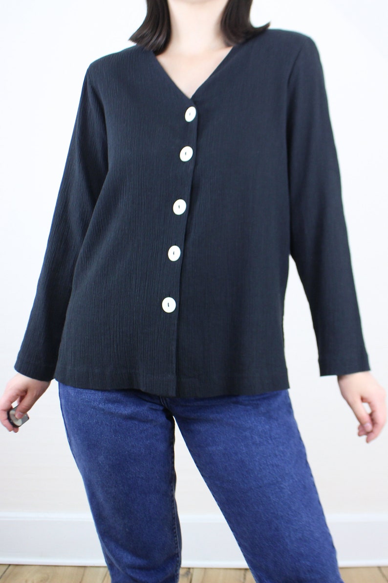 May include: A black long-sleeved button-up shirt with a v-neck and white buttons.