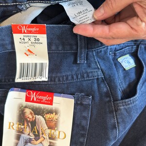 Może przedstawiać: Dżinsy z ciemnoniebieskiego denimu z metką Wrangler. Na metce widnieje napis "MSRO1NW 14 X 30 NIGHT SHADOW SHORT". Dżinsy mają luźny kr&oacute;j i zwężane nogawki.