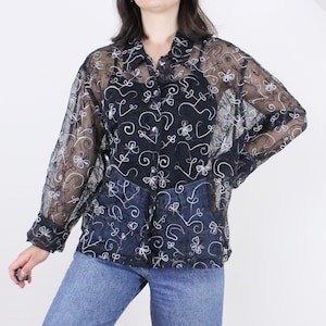 May include: A black sheer button-up shirt with white embroidered floral designs. The shirt is semi-transparent and has long sleeves.