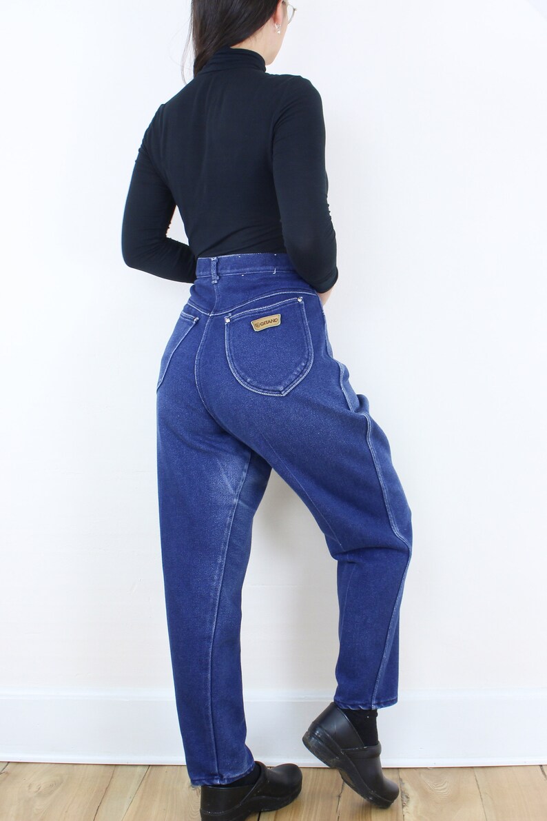 May include: A pair of high-waisted blue denim jeans with a brown leather patch that says "Wrangler" on the back pocket.