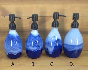May include: Four ceramic soap dispensers with a blue and white watercolor design. Each dispenser has a black pump and a rounded, teardrop shape. The base of each dispenser is a deep blue, with the color fading to white.