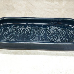 May include: A teal blue ceramic oval dish with a raised white design of swirling circles and dots.