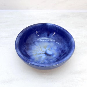 May include: A small, blue ceramic bowl with a white and blue marbled design. The bowl is perfect for holding small items like jewelry or keys.