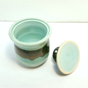 May include: A ceramic butter dish with a lid. The dish is light blue with a brown stripe around the middle. The lid is also light blue.