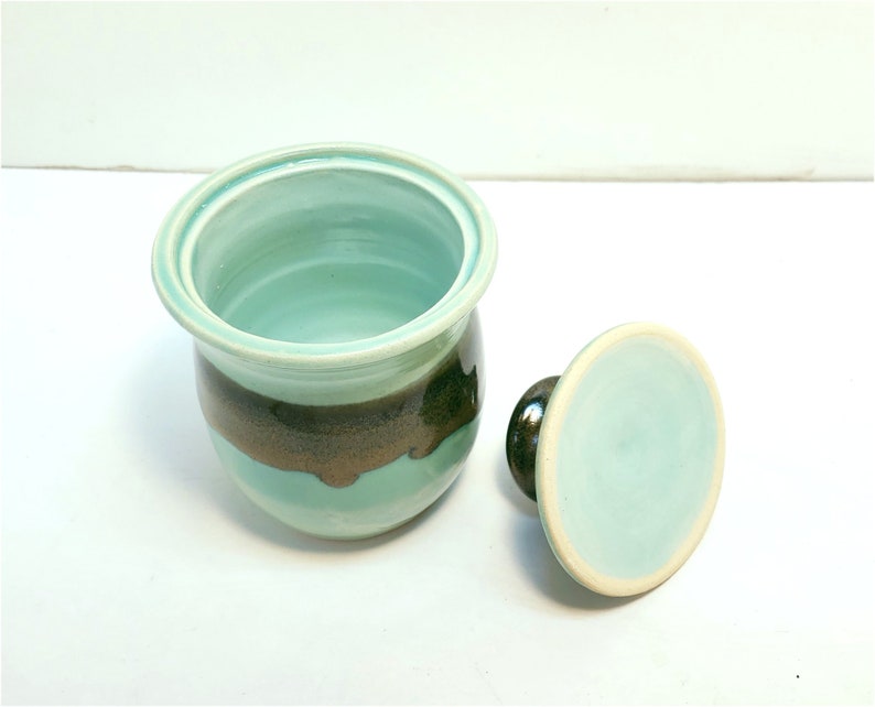 May include: A ceramic butter dish with a lid. The dish is light blue with a brown stripe around the middle. The lid is also light blue.