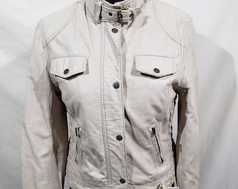 Puede incluir: Chaqueta de cuero beige claro con cuello alto y cierre de hebilla en la cintura. La chaqueta tiene dos bolsillos en el pecho, dos bolsillos laterales y costuras decorativas. La chaqueta se exhibe en un maniquí negro.
