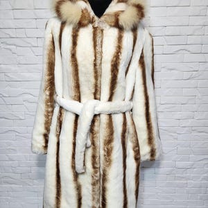 Women&#39;s fur coat made of warm, reliable faux fur. Warm brown-beige women&#39;s fur coat with a hood and belt.