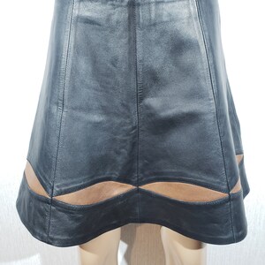 May include: Black leather skirt with a brown wavy hem design. The skirt has an A-line shape and is made of smooth leather. The skirt is displayed on a mannequin.