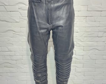 May include: Black leather pants with a belt and silver buckle. The pants have ribbed detailing on the lower legs and a zipper on the side. The pants are displayed on a mannequin.