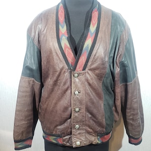 May include: A vintage leather jacket with a brown body, black sleeves, and a patterned collar and hem. The jacket has a button-up front and is displayed on a mannequin. The collar and hem feature a colorful geometric design.