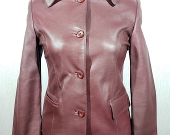 Puede incluir: Chaqueta de cuero burdeos con un diseño clásico. La chaqueta presenta un cuello, cierre de tres botones y dos bolsillos delanteros. La chaqueta se exhibe en un maniquí sobre un fondo blanco.