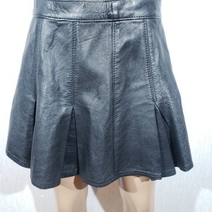 May include: A black leather skirt with a flared A-line silhouette. The skirt features vertical seams and pleats at the front, creating a structured and stylish look. The skirt is displayed on a mannequin.