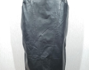 May include: A black leather skirt with a high waist and a knee-length hem. The skirt has a fitted shape with vertical seams and a small pocket detail. The leather has a slight sheen.