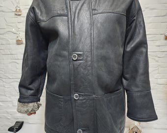 May include: A black leather jacket with a shearling collar and cuffs. The jacket has a button-up front, two front pockets, and a classic design. The jacket is a dark gray color and appears to be well-worn.