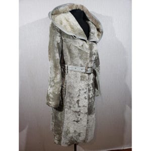 May include: A long, hooded coat in a mottled light grey and beige colour palette. The coat features a thick, textured exterior with a visible plush lining inside the hood. A matching belt with a rectangular metal buckle cinches the waist.