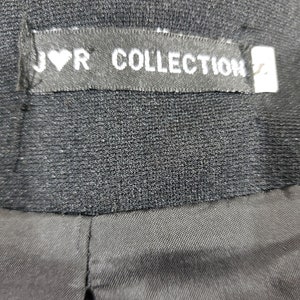 以下が含まれることがあります： 「J♡R COLLECTION」と書かれたラベルが付いた黒い衣服のクローズアップ。 ラベルは長方形で、白い文字とハートのシンボルが付いています。 衣服は、テクスチャード加工された生地で作られているようです。