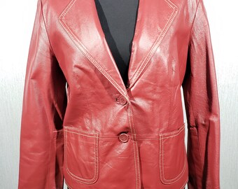 May include: A red leather blazer with a notched collar, two front pockets, and two buttons. The blazer has white stitching along the seams and around the pockets. The jacket is displayed on a black mannequin.