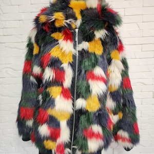 Könnte beinhalten: Eine langärmelige Jacke aus Kunstfell mit einem mehrfarbigen Muster aus roten, gelben, dunkelgrünen, marineblauen und weißen Flecken. Die Jacke verfügt über eine große Kapuze, einen silberfarbenen Reißverschluss in der Mitte und dunkle Rippbündchen.