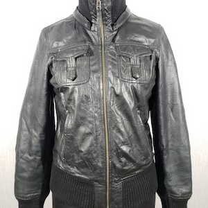 May include: Black leather jacket with a ribbed knit collar, cuffs, and hem. The jacket features a zip-up front, two chest pockets with flaps, and two side pockets. The jacket is displayed on a mannequin against a white background.