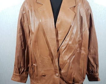 May include: A tan leather jacket with a double-breasted design. The jacket has a notched collar, two front buttons, and a tailored fit. The sleeves have a gathered detail at the shoulders. The jacket is displayed on a mannequin.