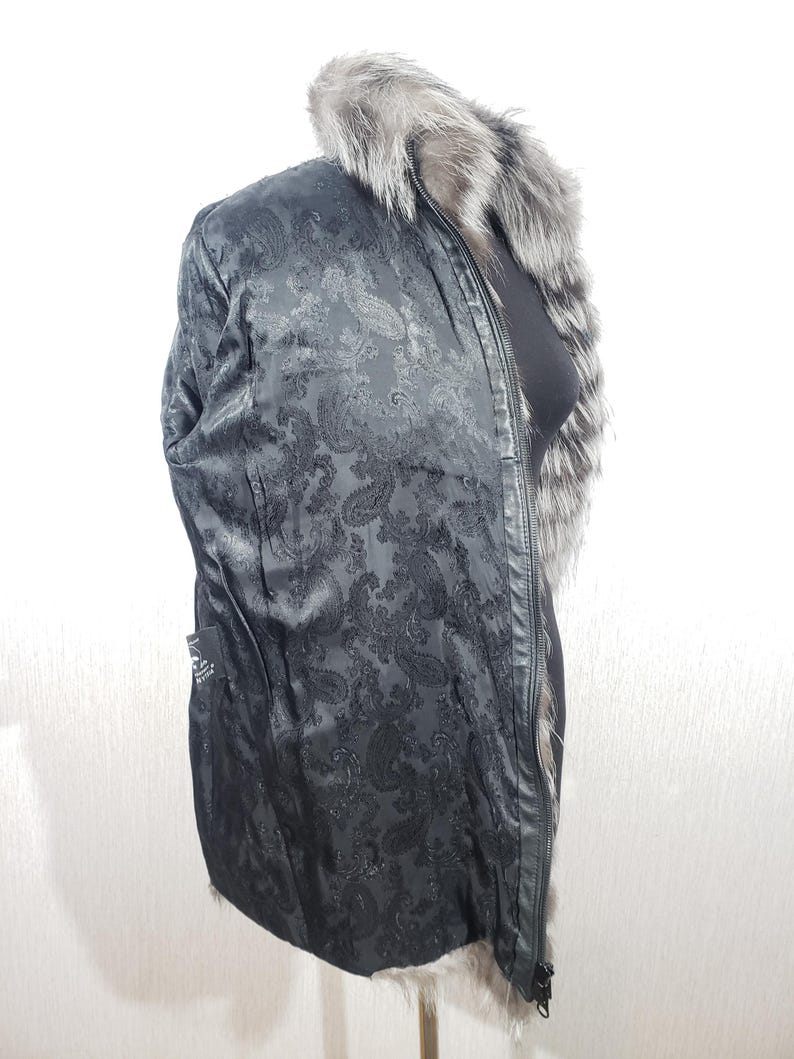 K&ouml;nnte beinhalten: Schwarze Jacke mit Paisley-Musterfutter und Pelzkragen. Die Jacke hat einen Rei&szlig;verschluss und eine schwarze Au&szlig;enseite. Der Pelzkragen ist grau und wei&szlig;. Die Jacke ist mittellang.