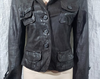 May include: A dark brown leather jacket with a classic design. It features a notched collar, three buttons, and four front pockets. The sleeves have buttoned cuffs, and one pocket has a buckle closure. The jacket is displayed on a mannequin.