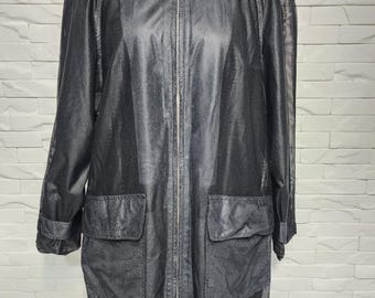 Può includere: Giacca nera in rete con chiusura a zip, due tasche frontali e collo. La giacca ha maniche lunghe e un design a rete sulle spalle e sull'orlo inferiore. La giacca è esposta su un manichino nero.