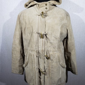 May include: A tan suede duffle coat with a hood and toggle closures. The coat has a faux fur lining in the hood and pockets on the front. The coat is displayed on a mannequin.