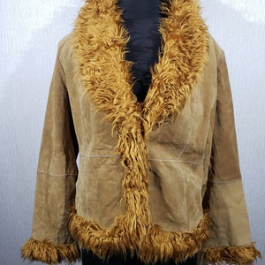 May include: A tan suede jacket with a faux fur collar and trim. The jacket is displayed on a black mannequin. The fur is a warm, golden brown colour, contrasting with the lighter tan of the suede. The jacket has a classic, vintage style.