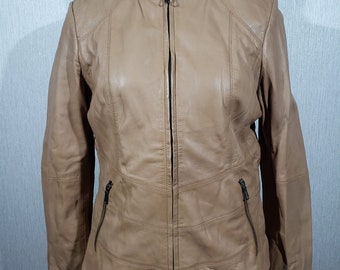 May include: A tan leather jacket with a stand-up collar and a full-length zipper. The jacket has two zippered pockets and stitched panels. The jacket is displayed on a black mannequin.