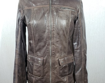 Könnte beinhalten: Braune Lederjacke mit Stehkragen, Frontreißverschluss und zwei Vordertaschen. Die Jacke hat ein leichtes Used-Aussehen und wird auf einer Schaufensterpuppe präsentiert.