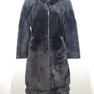 May include: A long black faux fur coat with a zip fastening and a notched collar. The coat has a textured finish and a layered design at the hem. The coat is displayed on a mannequin against a white background.