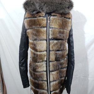 May include: A luxurious winter coat featuring a fur-lined hood and a body constructed with horizontal panels of brown fur. The coat has black leather sleeves and a full-length zipper. The fur trim around the hood is a darker shade of brown.