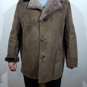 Peut inclure: Manteau en peau de mouton marron avec un large col et une fermeture à boutons. Le manteau a un design classique avec un aspect chaud et texturé. Les poignets sont garnis d'un matériau plus foncé et duveteux. Le manteau a deux poches avant.