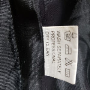 以下が含まれることがあります： 黒い生地のクローズアップ。白いタグには「WASH SEPARATELY PROFESSIONAL DRY CLEAN」を含む洗濯表示が記載されています。