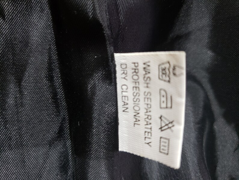 以下が含まれることがあります： 黒い生地のクローズアップ。白いタグには「WASH SEPARATELY PROFESSIONAL DRY CLEAN」を含む洗濯表示が記載されています。