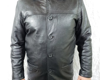 May include: A black leather jacket with a button-up front, a collar, and two front pockets. The jacket appears to be worn by a person. The jacket is a classic style, suitable for various occasions.