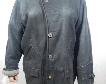 May include: A dark gray leather jacket with a shearling collar and cuffs. The jacket features a button-up front, two front pockets, and a buckle detail on the sleeve. The jacket is a classic style, suitable for cold weather.