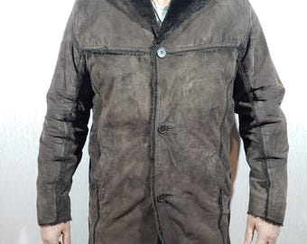 May include: A brown suede jacket with a black shearling collar and trim. The jacket has a button-up front and long sleeves. The jacket is a medium length and appears to be made of a soft material. The jacket is worn by a person.
