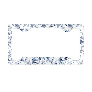 May include: A rectangular license plate frame featuring a white background with a repeating blue floral pattern. The frame has four circular mounting holes positioned at the corners, designed to secure a standard vehicle license plate.