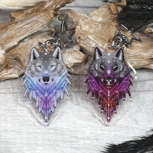 May include: Two wolf head keychains with a galaxy design. The keychain on the left has a blue and purple galaxy design. The keychain on the right has a pink and purple galaxy design.