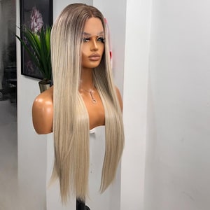 Könnte beinhalten: Eine lange, blonde Perücke mit dunklem Ansatz und einem geraden, glatten Stil. Die Perücke wird auf einem Schaufensterpuppenkopf mit Halskette präsentiert. Das Haar hat einen natürlich aussehenden Farbverlauf, der von dunkelblond zu hellblond übergeht.