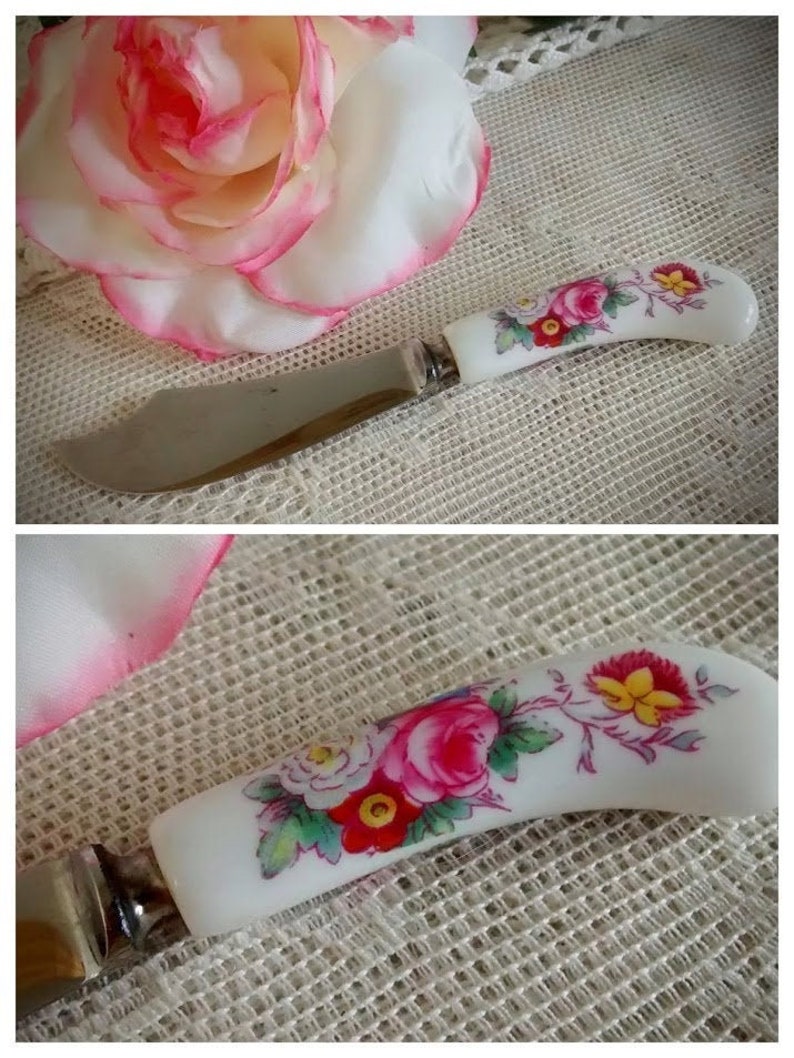 May include: A white butter knife with a floral design on the handle. The handle is decorated with pink, red, yellow, and green flowers. The knife is made of stainless steel.